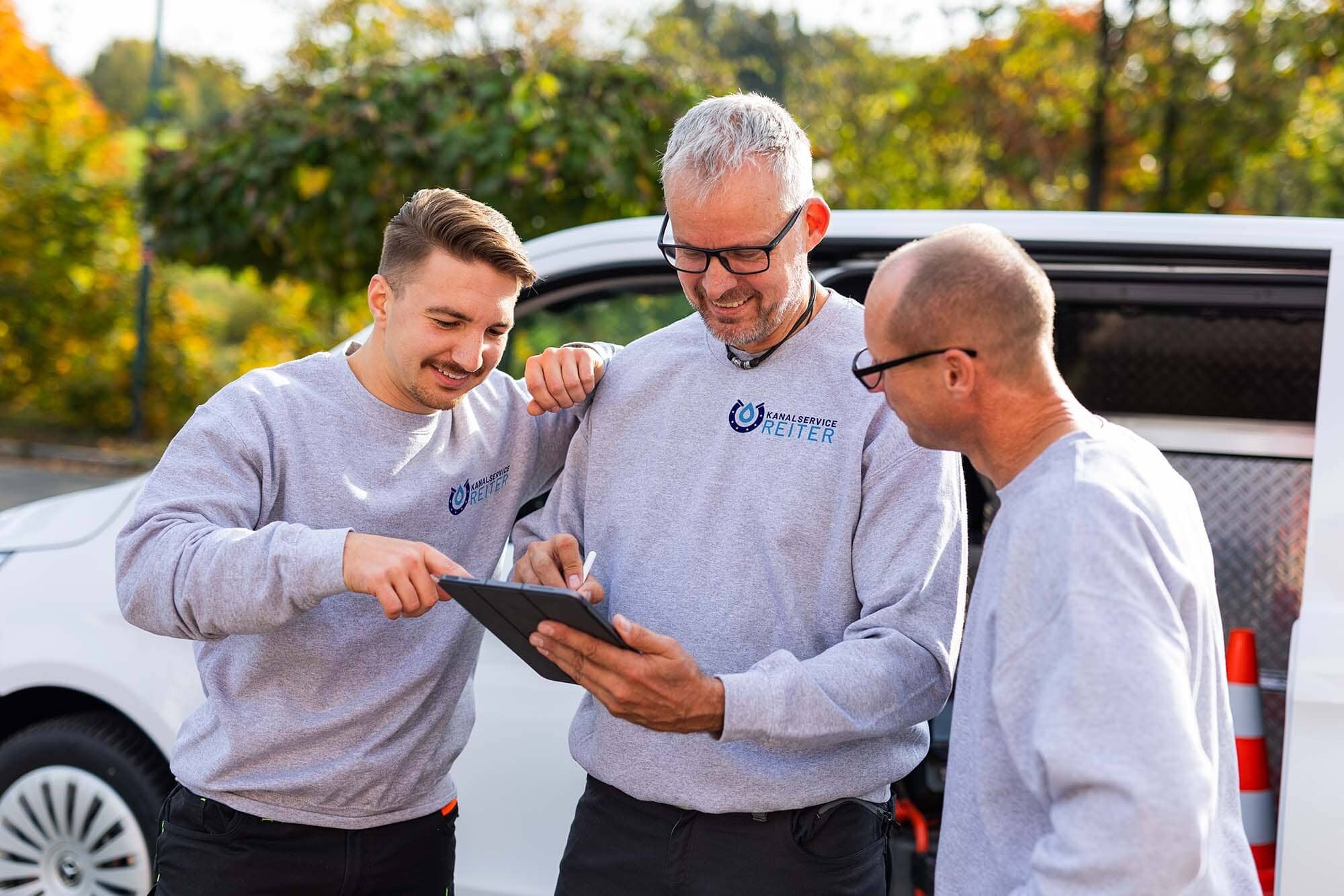 Drei Techniker von Kanalservice Reiter besprechen am Einsatzwagen einen Befund