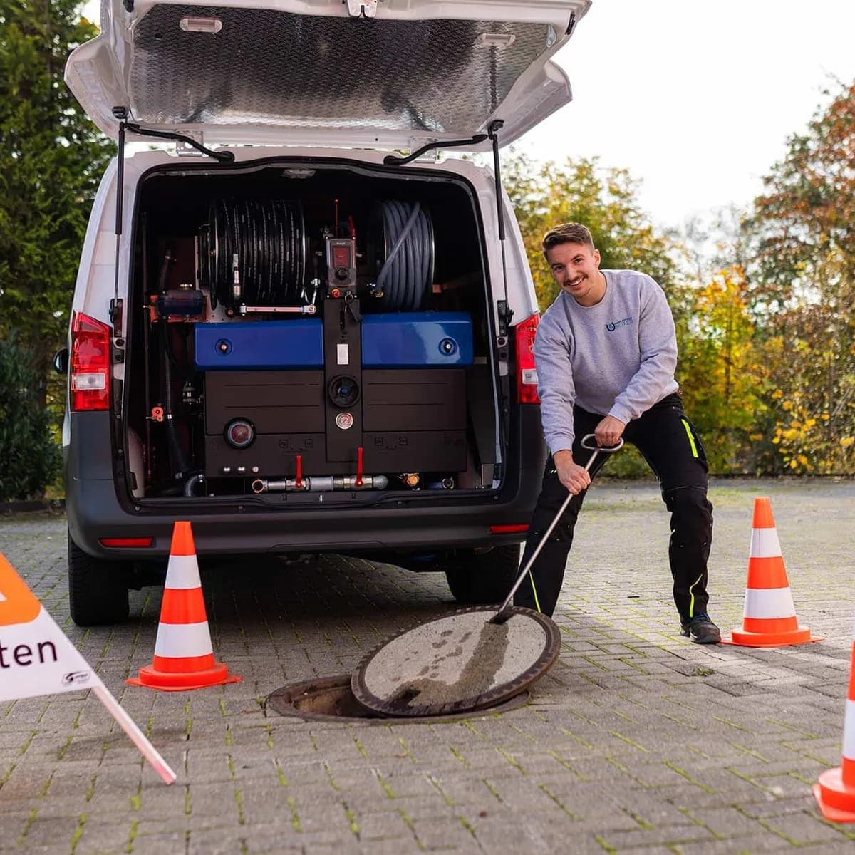 Techniker arbeitet mit abgesicherter Baustelle an einem Kanalschacht